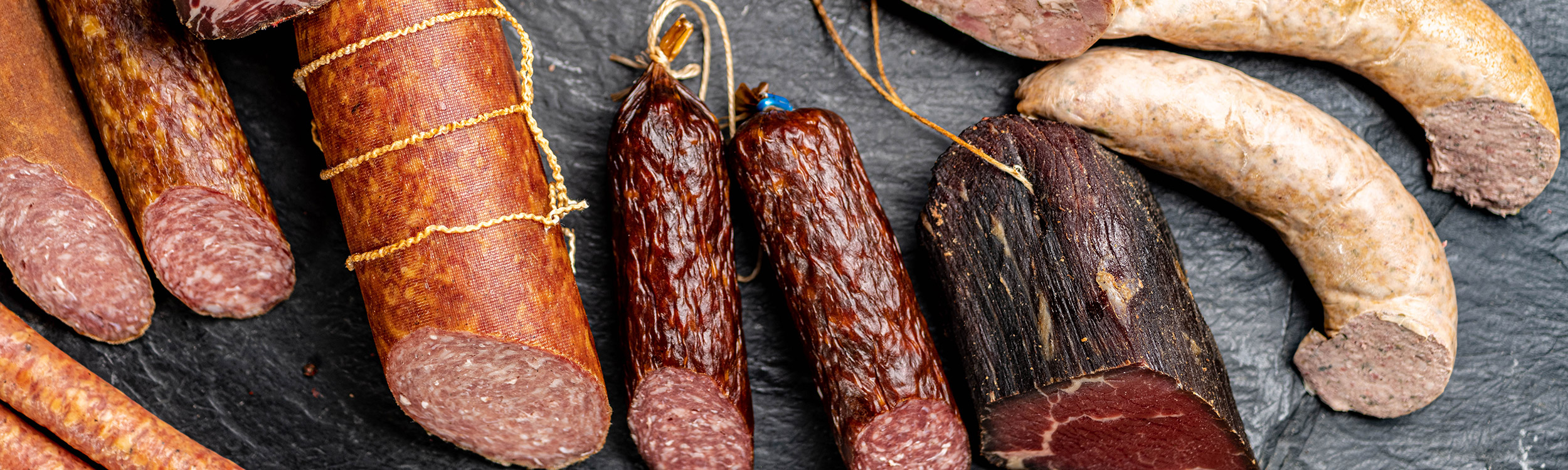 Das Bild zeigt verschiede Würste. Rotwurst, Salami und Leberwurst auf einer Schiefertafel.